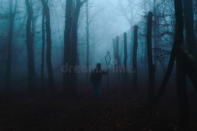 Man with a staff in an autumn forest in a fog in the evening