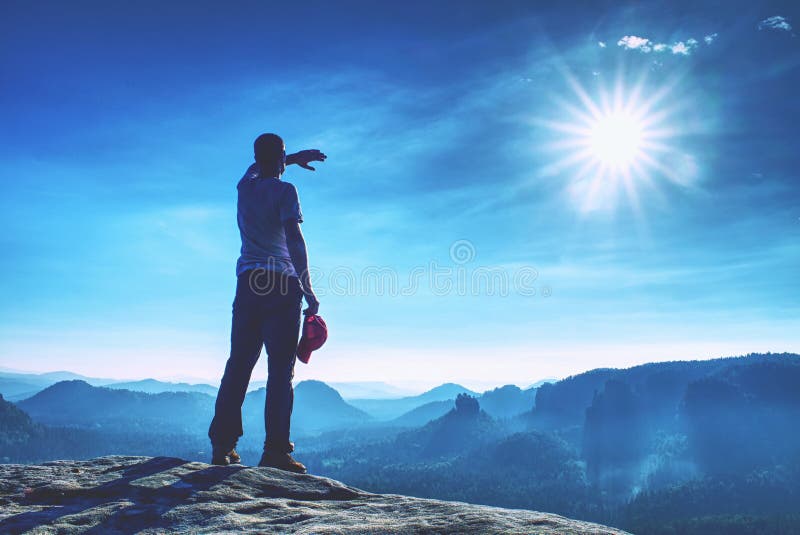Male hiker is stand on edge and enjoying dramatic overlook of misty landscape. The Sun is hidden in thick mist and change colors. Male hiker is stand on edge and enjoying dramatic overlook of misty landscape. The Sun is hidden in thick mist and change colors.