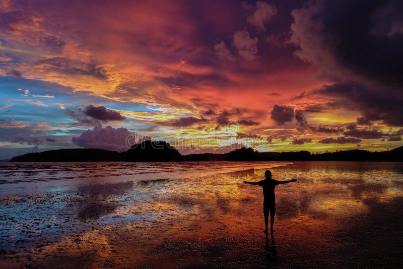 Silhouette of a man standing on the beach at beautiful colorful sunset in Thailand. Freedom concept.