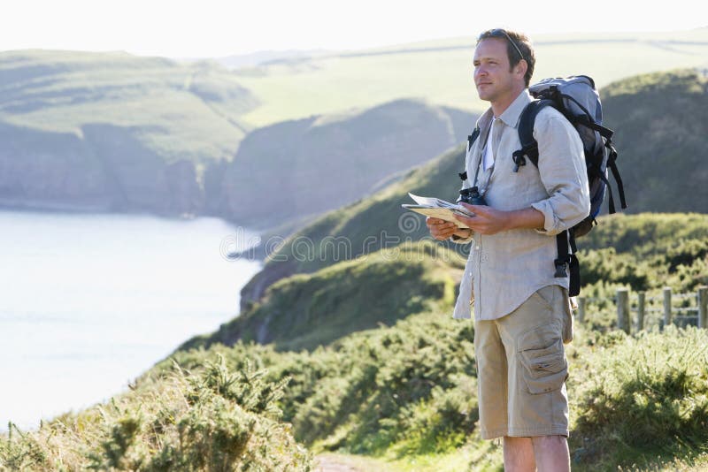 Man standing on cliff side path holding map