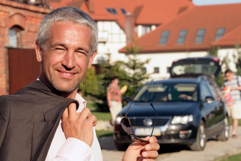 Handsome mature businessman standing before house. Family going on vacation.