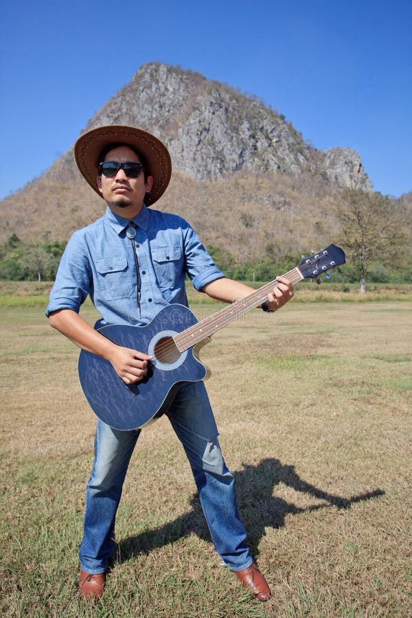 Man standing and playing folk guitar with mountain behind