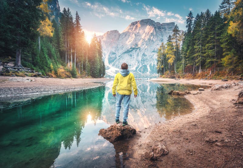 Man is standing on the stone on Braies lake at sunrise in autumn