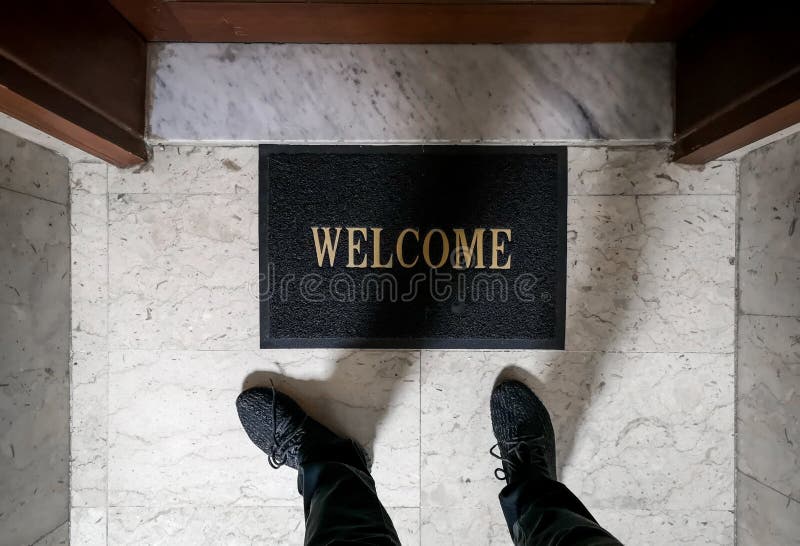 A man standing on top of a welcome floor mat in front of an apartment door