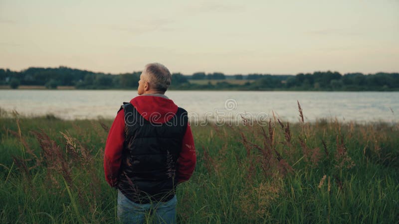 A man stands on the Bank of a river at sunset.