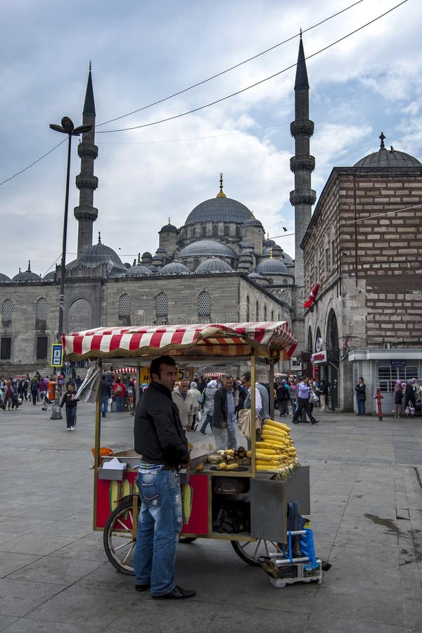 A man stands next to his mobile corncob cart in the Eminonu district of Istanbul in Turkey. In the background stands the 400 year old Yeni Cami (New Mosque).