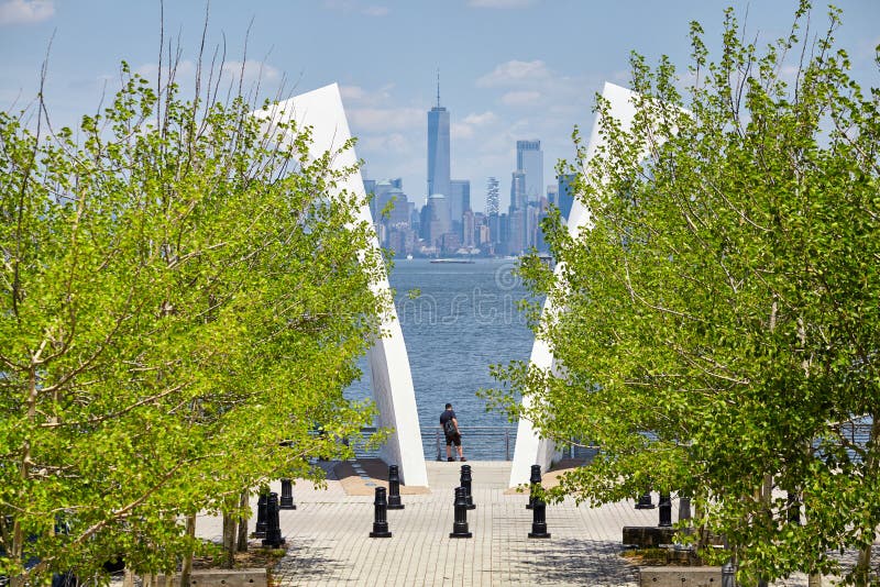 Man stands between Postcards, Staten Island September 11 Memorial with Manhattan in distance.
