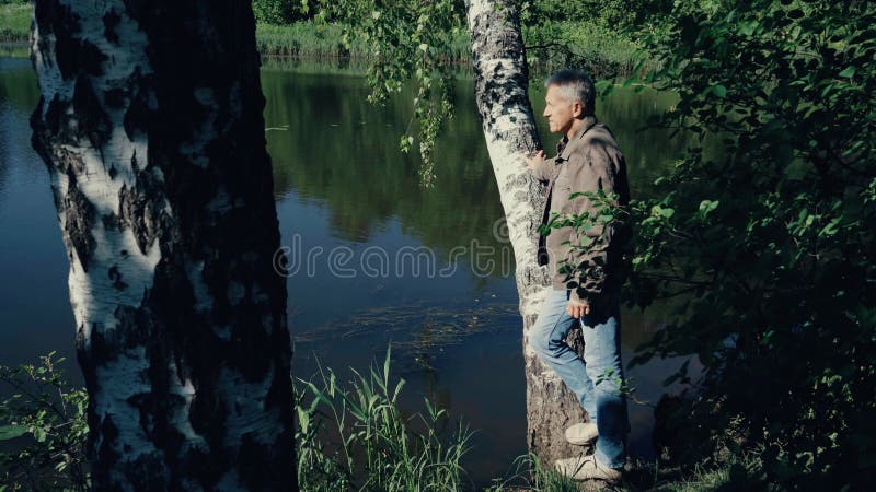 A man stands by the river and looks at the water on a summer day.