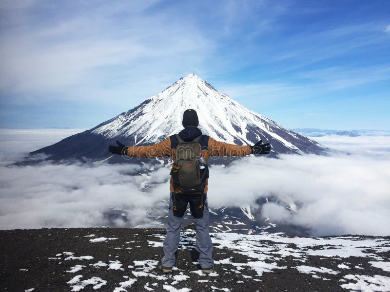 Man stands on the slope of the volcano with open arms