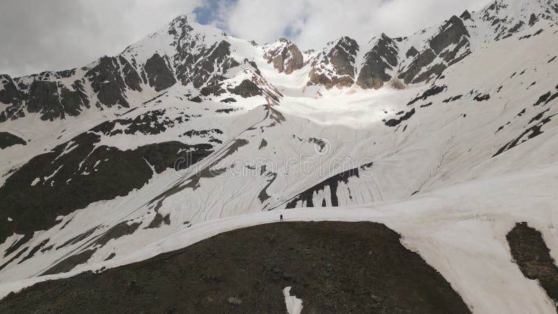 Man stands on snowy mountain peak, aerial selfie dronie. Stunning mountain scenery. Solo adventure in remote wilderness stock footage