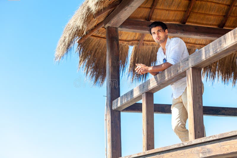 Man steht am Strand auf einem Holzhüttenbungalow am Meer lizenzfreies stockbild Man steht am Strand auf einem Holzhüttenbungalow am Meer lizenzfreies stockbild