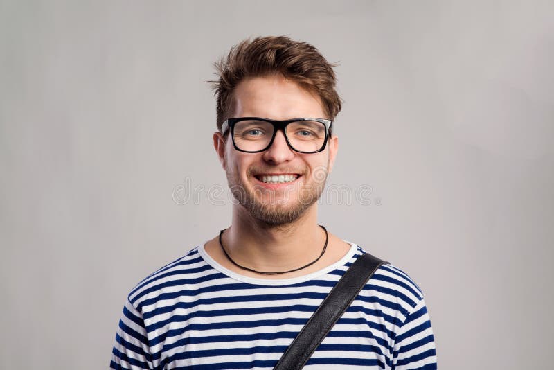 Man in striped t-shirt and eyeglasses against gray background.