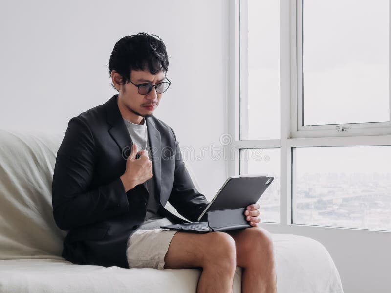 Man in a suit and glasses is sitting on a couch with a tablet in his lap royalty free stock photography