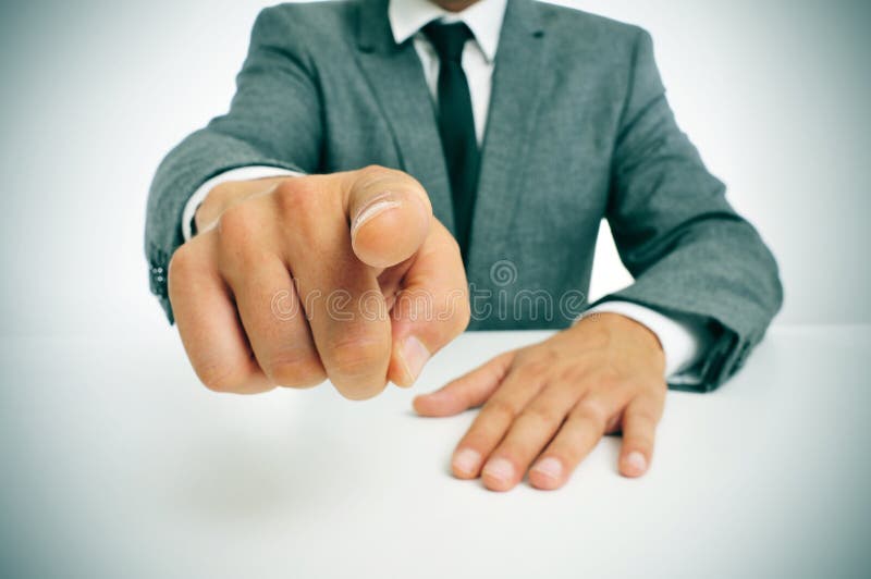 Hombre agotador un traje en mesa muestra dedo sobre el observador.