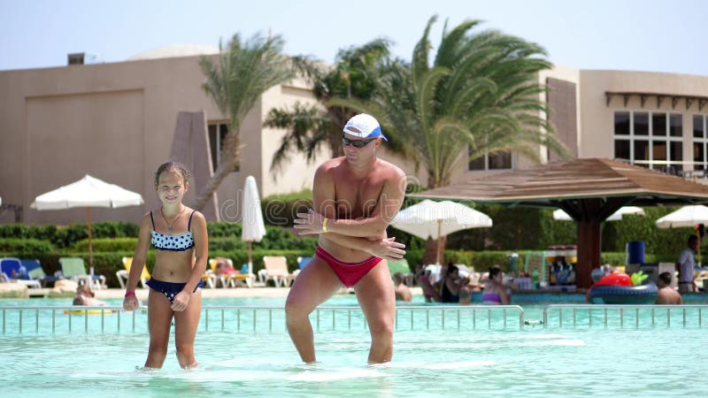 Man in sun glasses, father and daughter, kid girl, dancing in the pool water, having fun together. Happy family relaxing