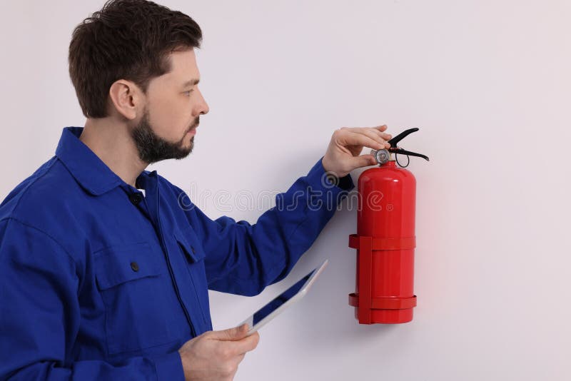 Man with tablet checking fire extinguisher indoors stock photos
