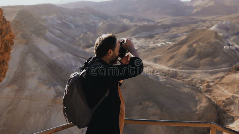 Man takes photos of amazing desert landscape. European male tourist with camera at massive mountain view. Israel 4K.