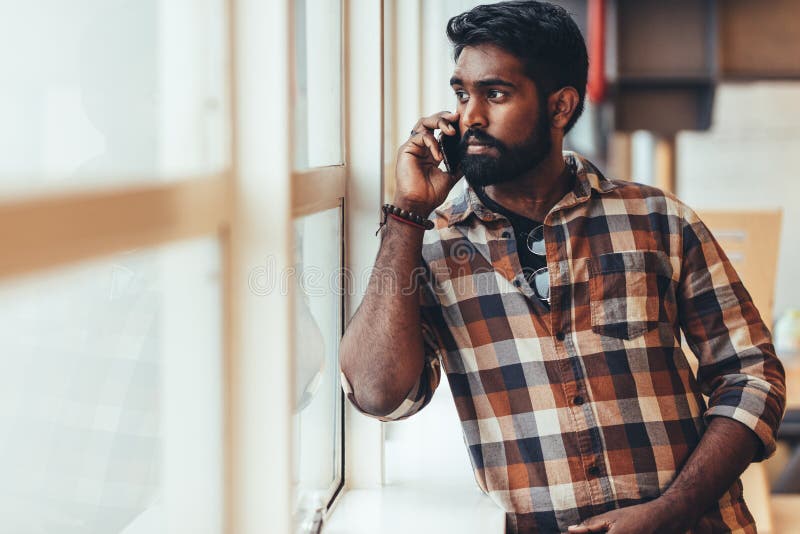 Man talking over mobile phone standing beside a window