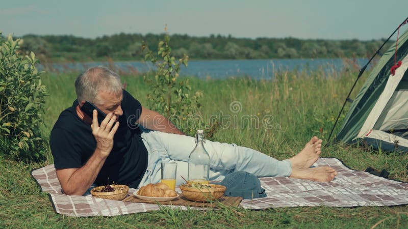 A man speaks on the phone while relaxing in nature.