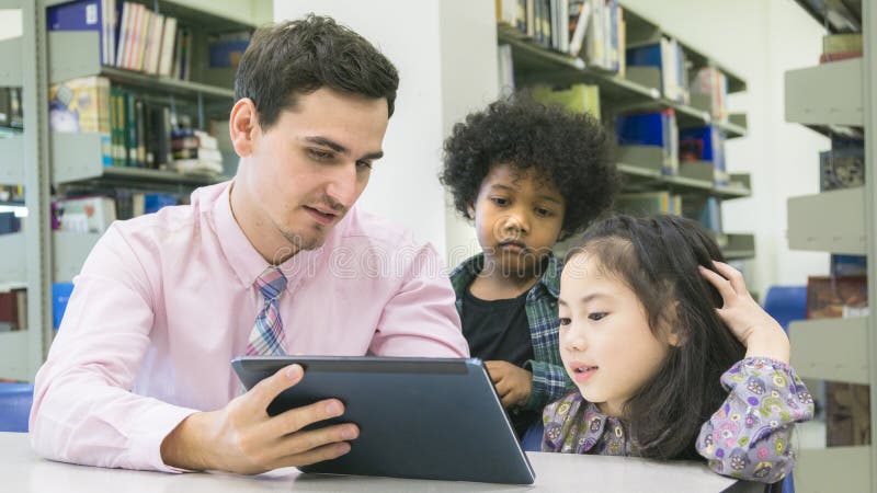 man teacher and kid student learning and looking on tablet device with self book in the background