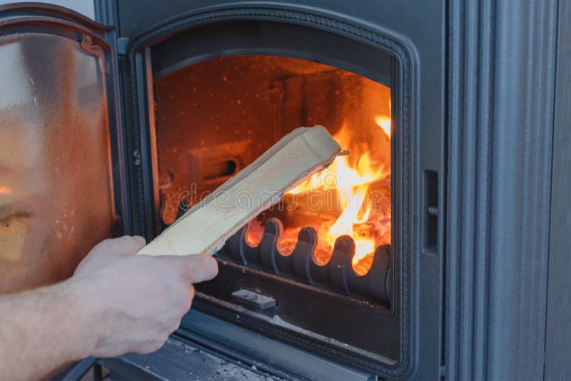 A man throws firewood into a cast-iron stove-fireplace. Close-up view.