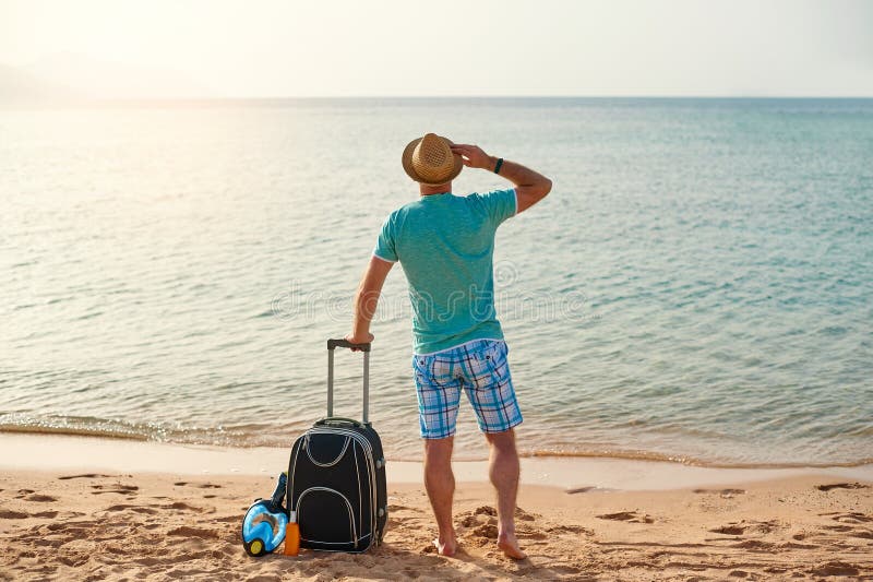 Man tourist in summer clothes with a suitcase in his hand, looking at the sea on the beach, concept of time to travel stock photography Man tourist in summer clothes with a suitcase in his hand, looking at the sea on the beach, concept of time to travel stock photography