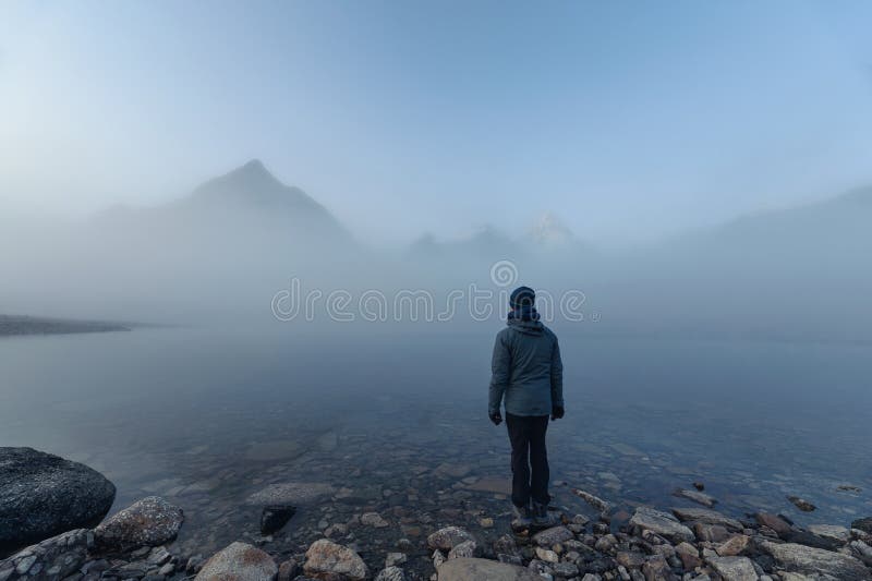 Man traveler standing on Lake Magog with Mount Assiniboine in foggy at provincial park