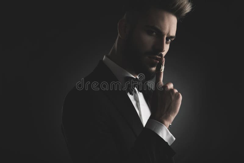 Man in tuxedo hushing with finger at lips