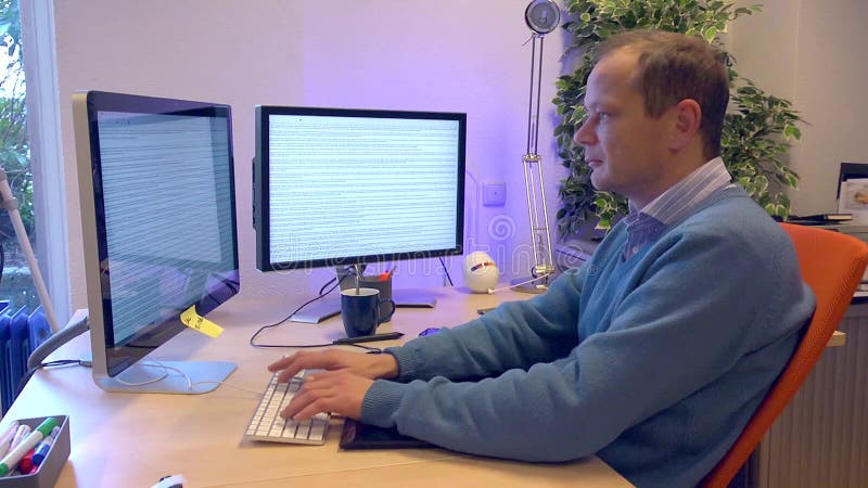 Man typing behind a computer with two screens