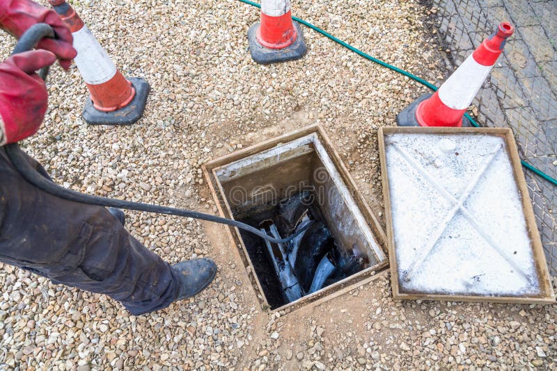Man unblocking sewage drain through open inspection chamber, UK