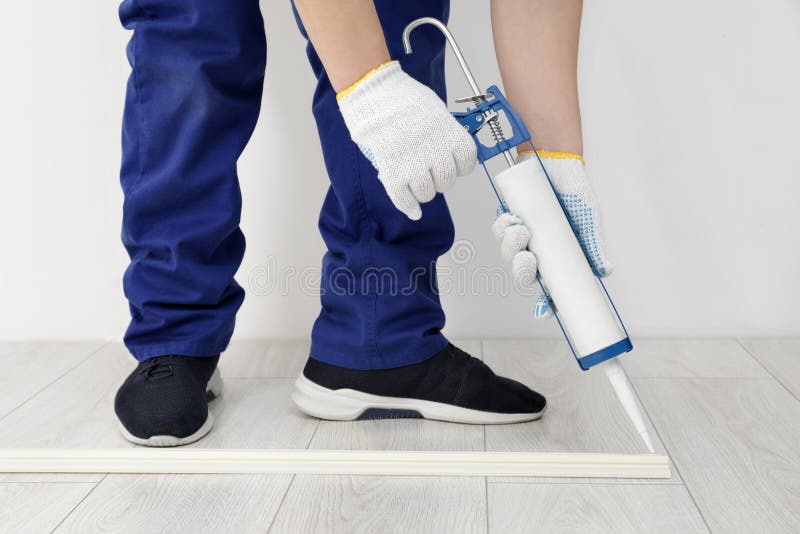 Man Using Caulking Gun while Installing Plinth on Laminated Floor in