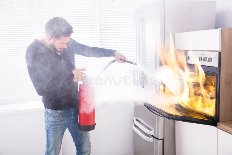 Man Using Fire Extinguisher To Stop Fire Coming From Oven