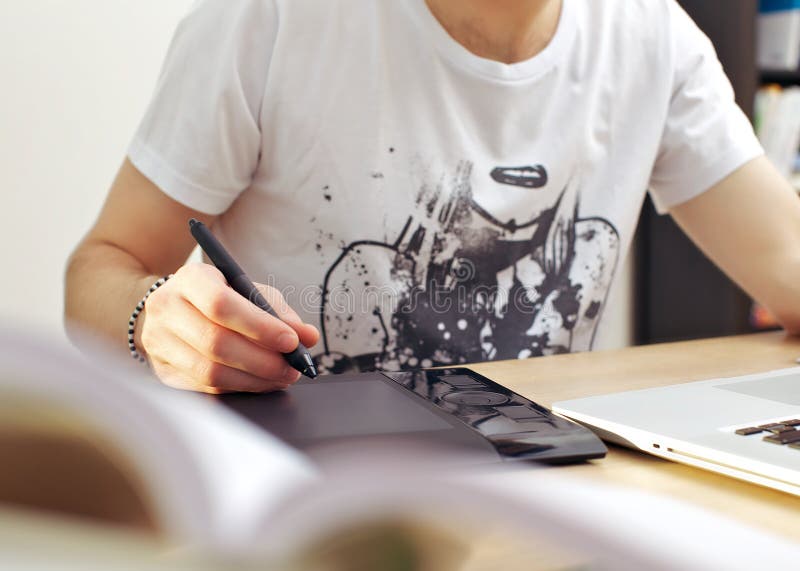 Man using graphics tablet while seated in front of his laptop at a desk.