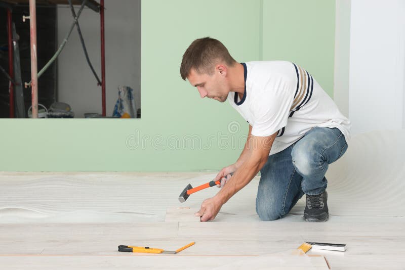 Man Using Hammer during Installation of New Laminate Flooring in Room