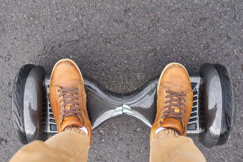 Close up of man using hoverboard on asphalt road. Feet on electrical scooter outdoor, top view