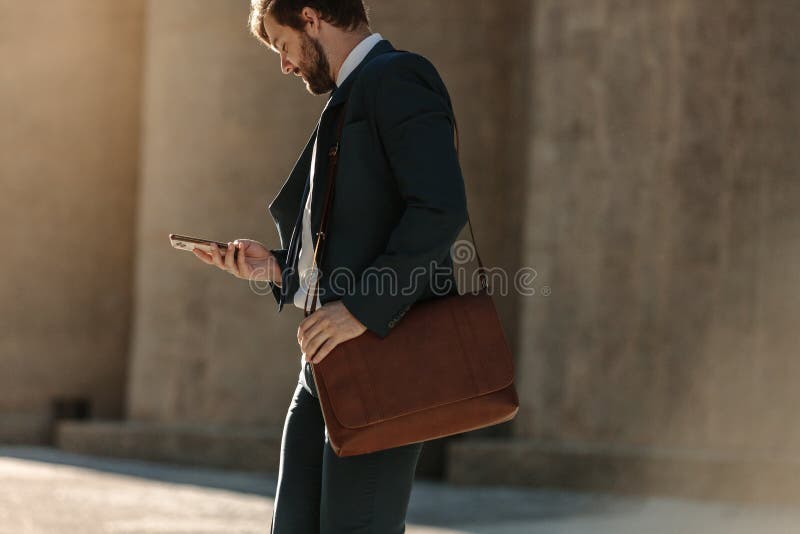 Men in formal clothes commuting to office early in the morning carrying  office bags. Businessman using mobile phone while walking on city street to  of Stock Photo - Alamy