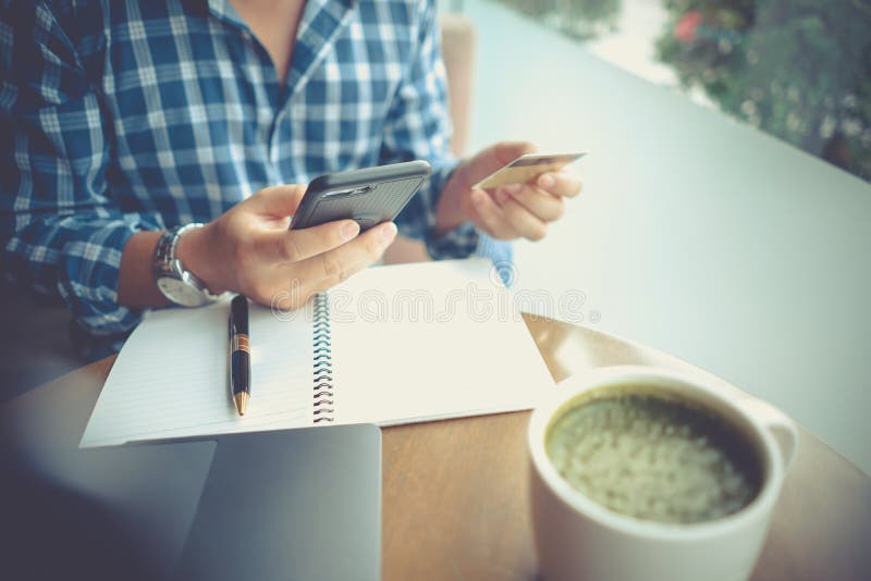 Man using mobile smartphone and credit card for online shopping in coffee shop, laptop computer notebook and coffee cup on table. stock photography Man using mobile smartphone and credit card for online shopping in coffee shop, laptop computer notebook and coffee cup on table. stock photography