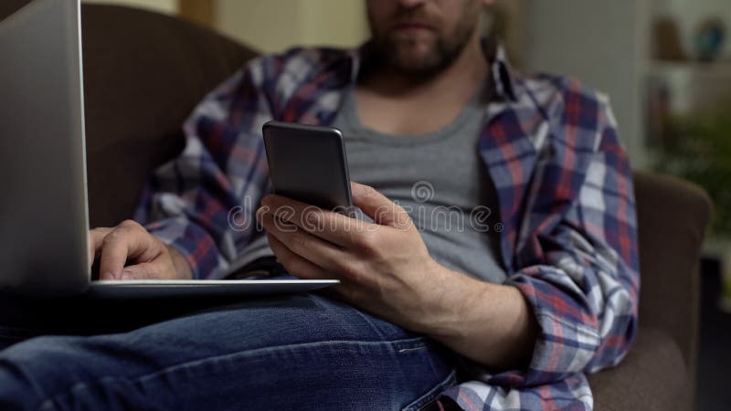 Man using phone application and working on laptop, online payment confirmation stock photo