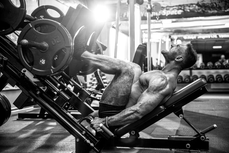 Man Using A Press Machine In A Fitness Club. Strong man doing an exercise on its feet in the simulator. stock photos Man Using A Press Machine In A Fitness Club. Strong man doing an exercise on its feet in the simulator. stock photos