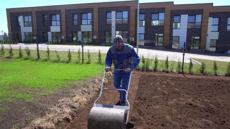 man is using roller to harden ground soil for lawn sowing. Gimbal movement