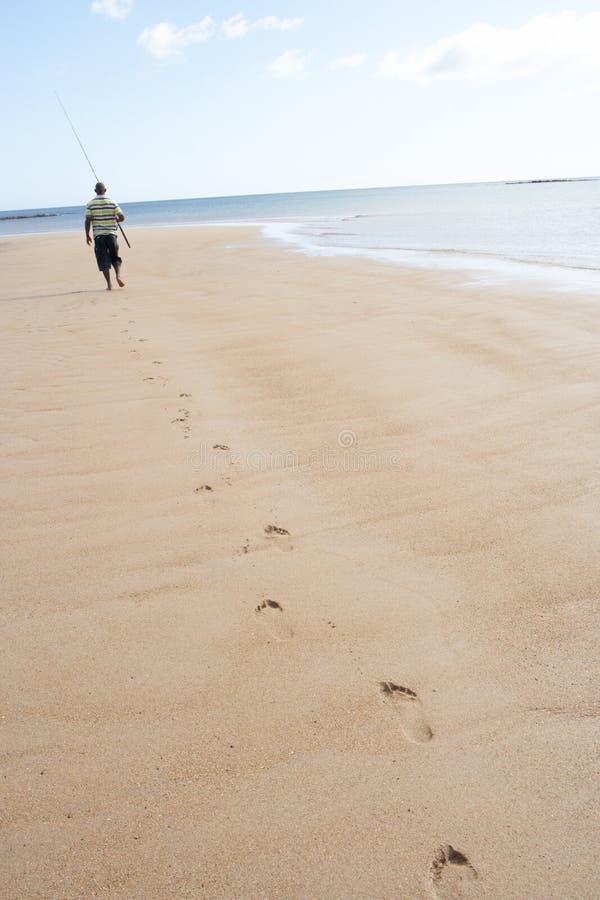 Man Walking Along Shore Carrying Fishing Rod