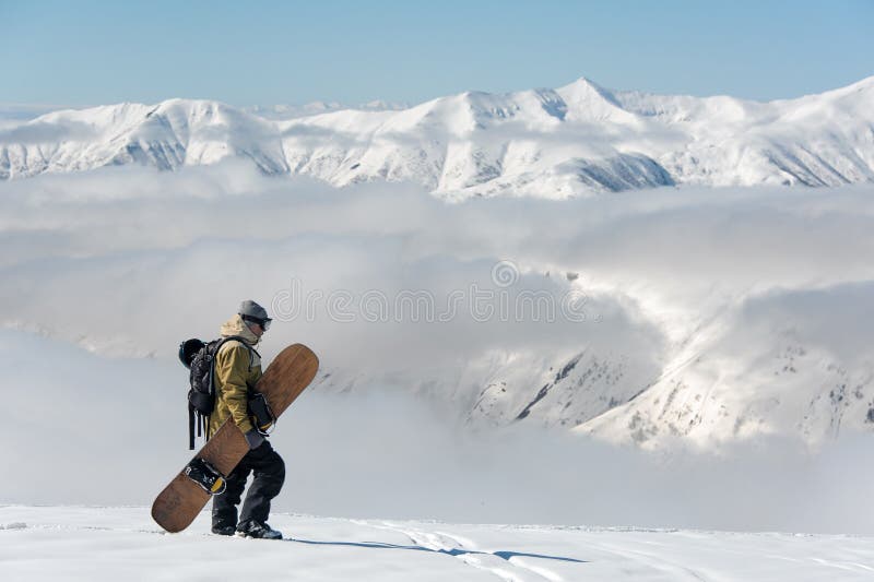 Man walking with the brown snowboard in the mountain resort