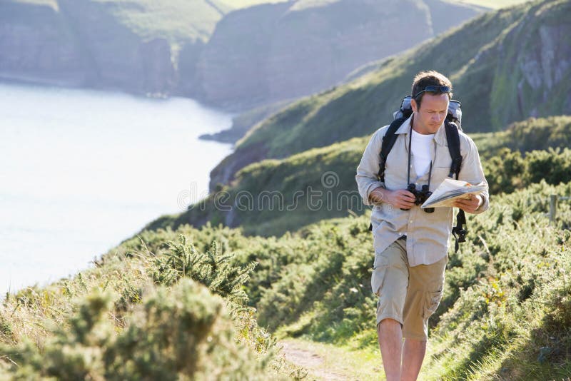 Man walking on cliff side path looking at map