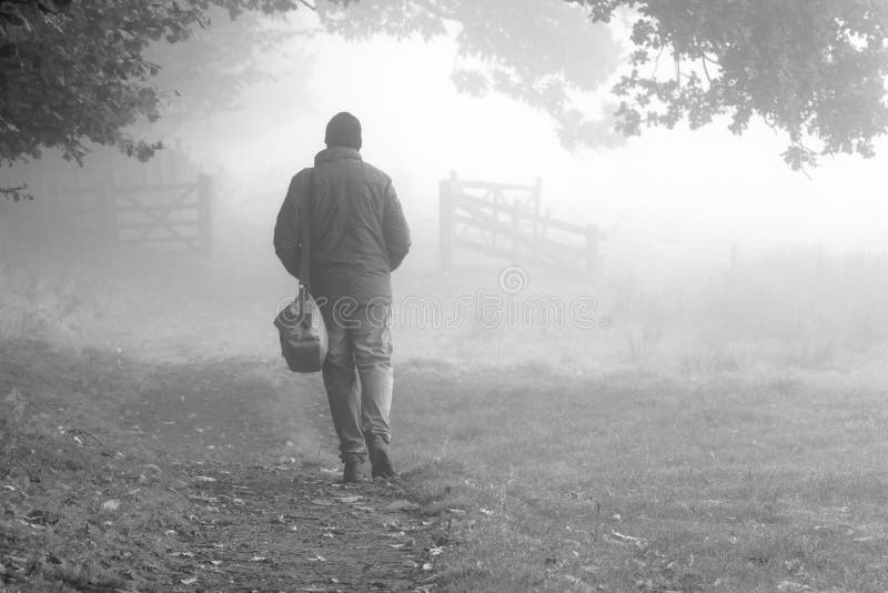 Fotografia di un uomo che cammina in un giorno di nebbia in campagna.