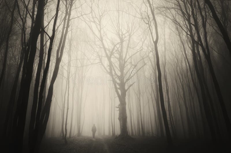Creepy man walking in spooky forest with fog on Halloween