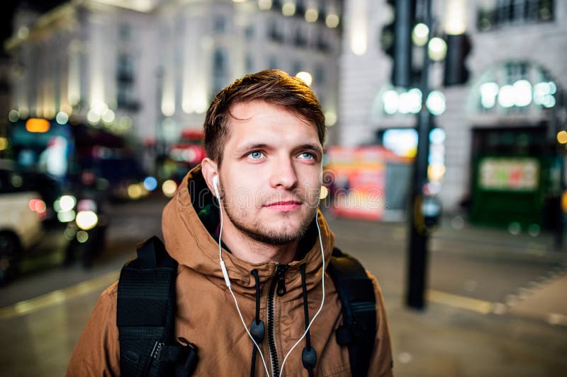 Man walking in the streets of London at night. Young hipster man with earphones, listening music, walking in the streets of London at night stock photo Man walking in the streets of London at night. Young hipster man with earphones, listening music, walking in the streets of London at night stock photo