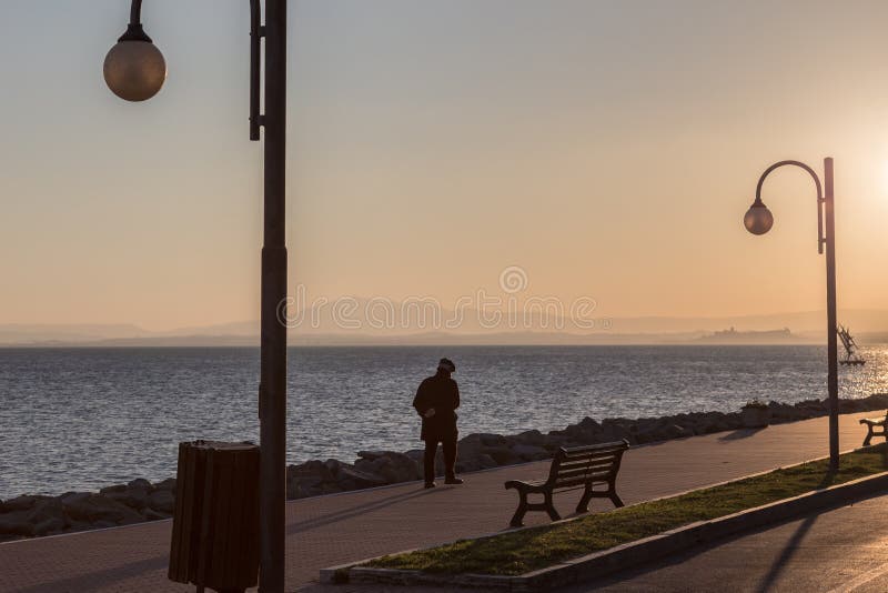 Siluetu muža s dlhými tieň prechádzky pri jazere, smerom na západ slnka.