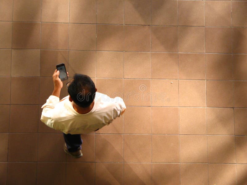 Man walking and texting on mobile phone, aerial view. Aerial view of a man walking and turn using his mobile phone for text messages, cell phone or smartphone. Hispanic or Latino man using device to communicate.