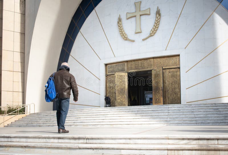 A man walks towards the open door of an Orthodox church in Tirana. Above the door is a large cross and ears of gold in Albania