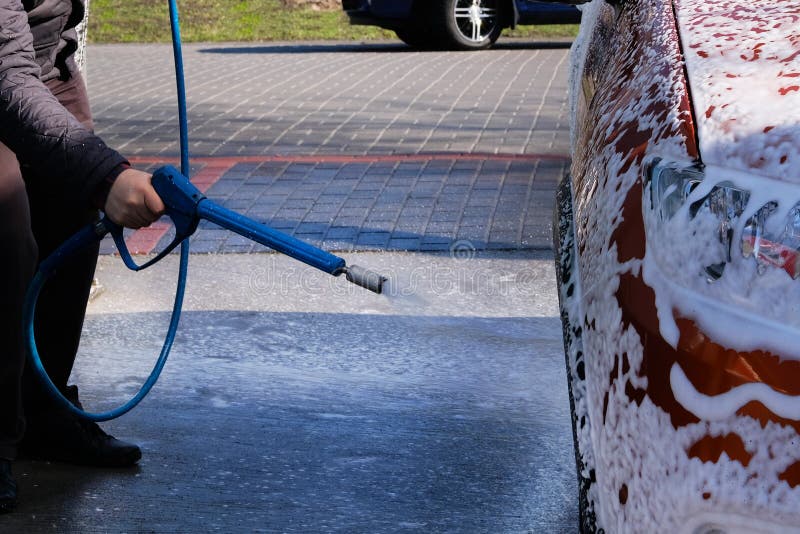 Man washes his orange car at car wash. Cleaning with soapy at self-service car wash. Soapy water runs down. Male hand and car body close up.